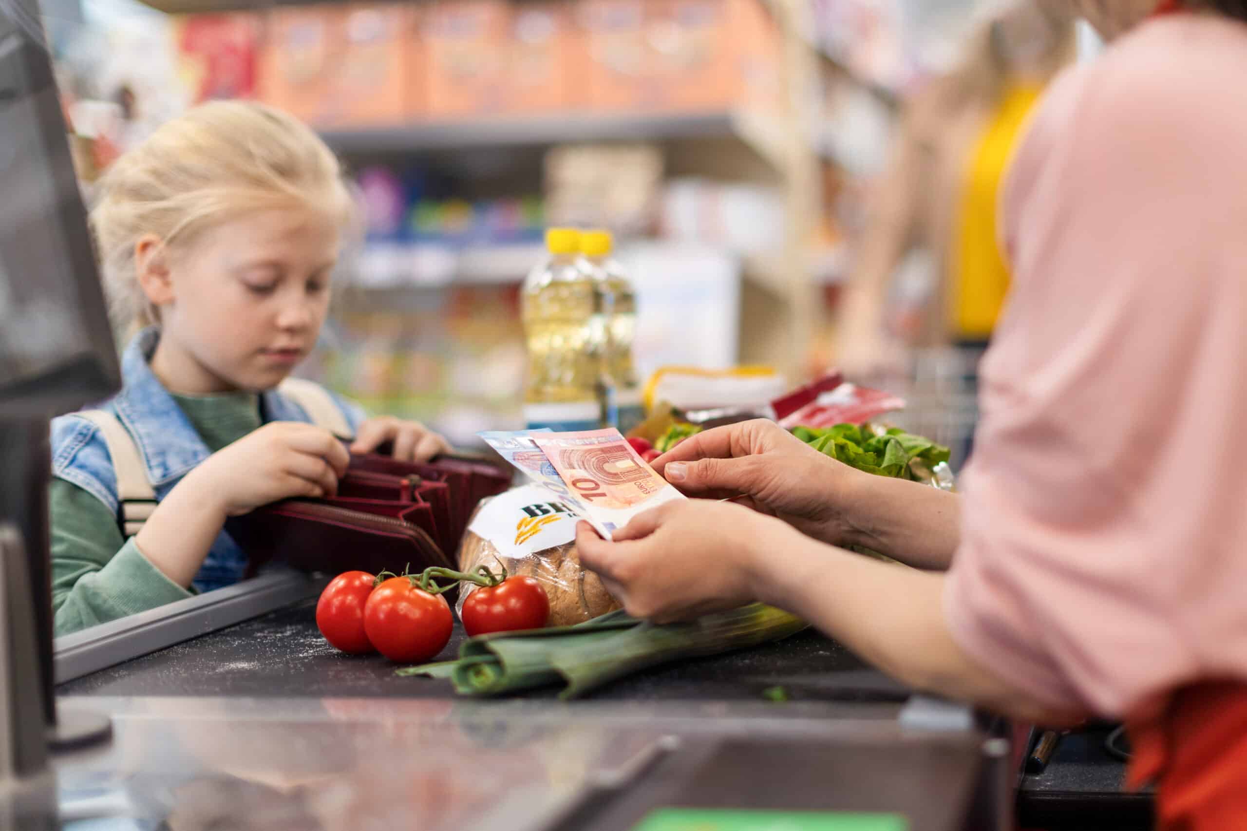 Nahaufnahme eines kleinen blonden Mädchens, das im Supermarkt für den Lebensmitteleinkauf bezahlt. Nahaufnahme eines kleinen blonden Mädchens, das im Supermarkt für den Lebensmitteleinkauf bezahlt.